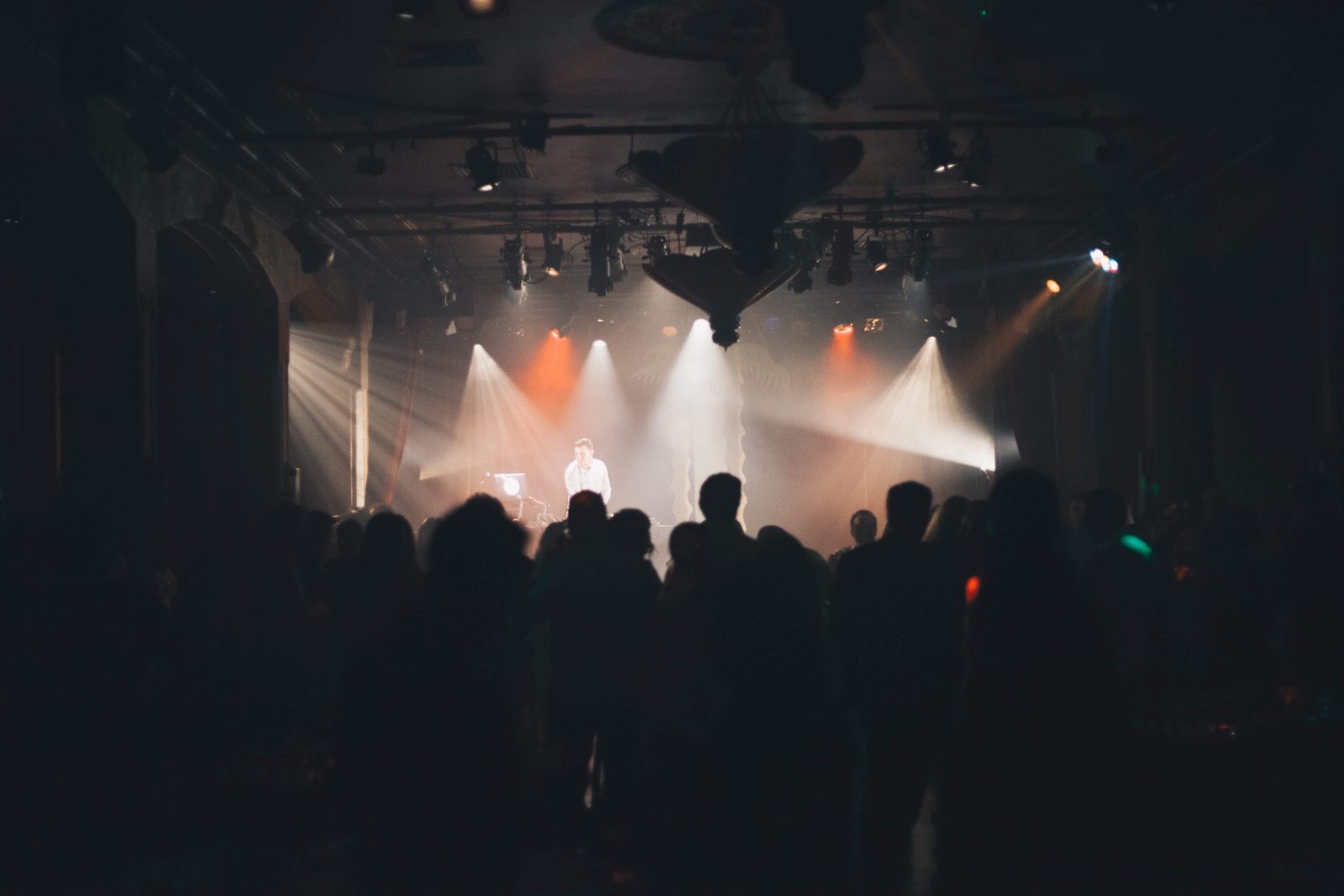 Guests silhouetted in front of the stage as white and amber beams cut through haze