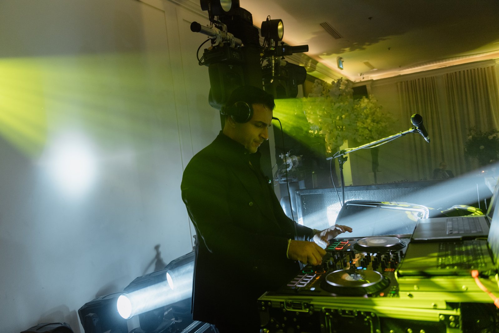 MAJD in headphones working the decks under green beams and moving heads at a destination celebration