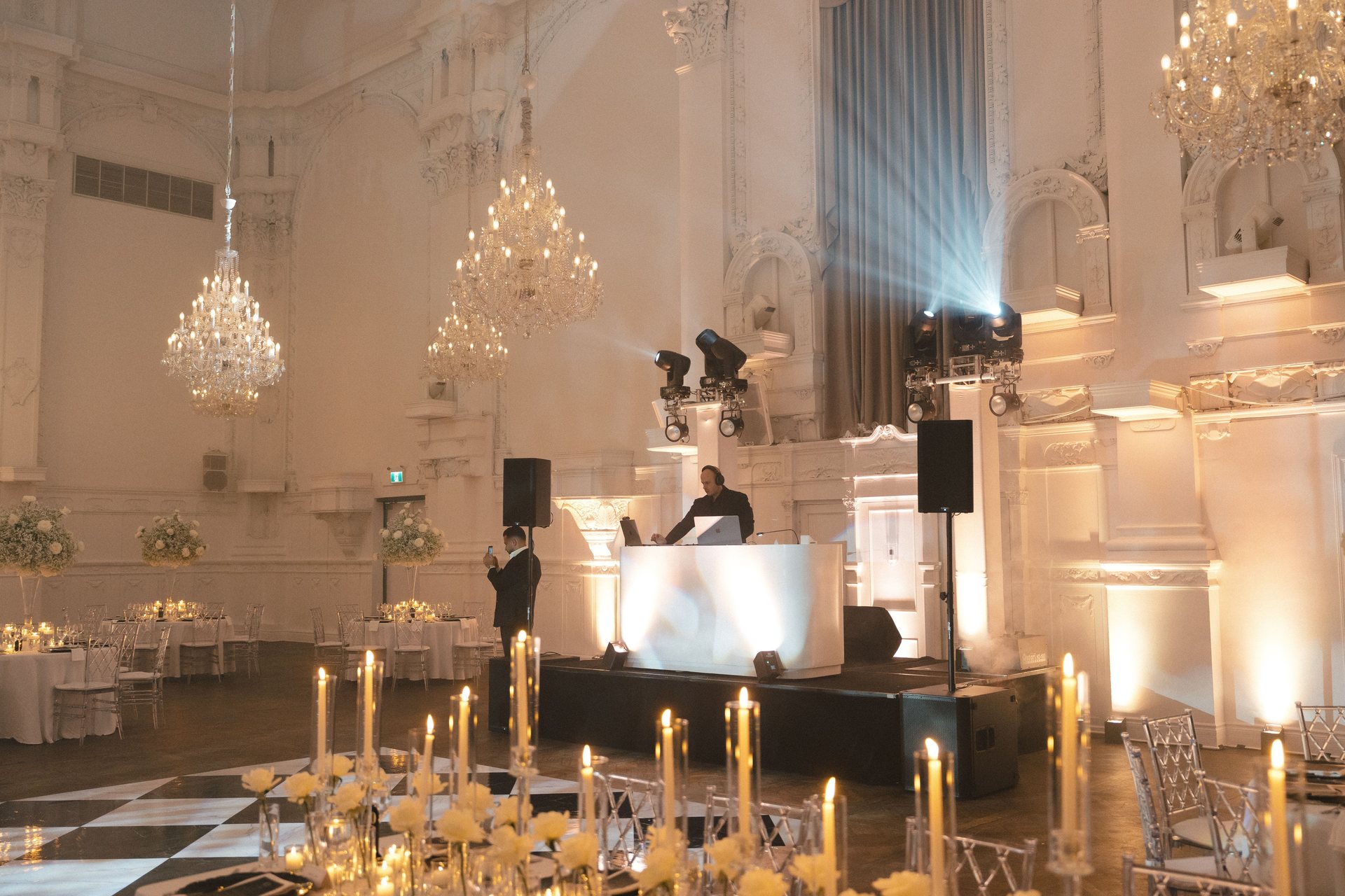 MAJD behind a white DJ booth in a chandelier-lit heritage ballroom set with candlelit tables, moments before doors open