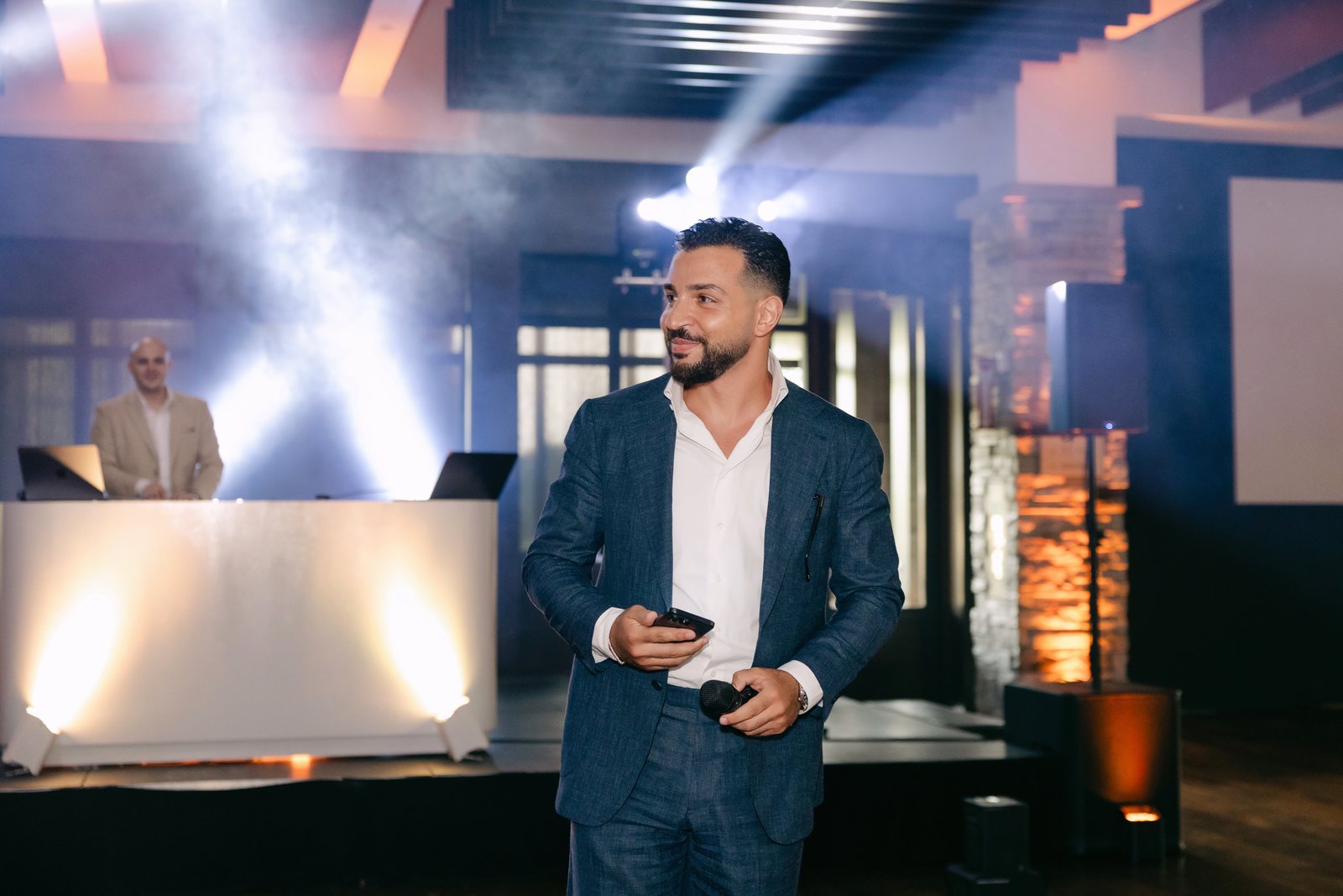 MAJD in a tailored blue suit, microphone in hand, hosting the room as MC