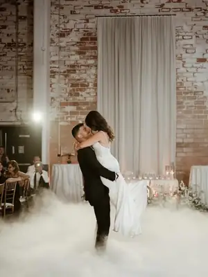 The groom lifting the bride during their first dance as low fog rolls across the floor