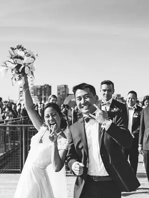 The bride raising her bouquet as the couple walk out past cheering guests